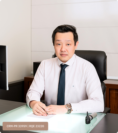 Dr. Denis M. Ueda em seu consultório, vestindo jaleco branco